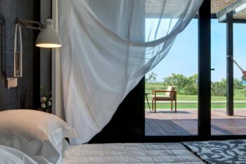 Bett mit Blick in den Garten mit weißem Vorhang und moderner Einrichtung