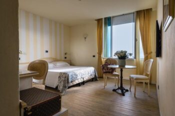 Hotelzimmer mit heller Tapete, Doppelbett und offenem Fenster