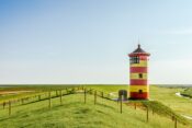 Rot-gelber Leuchtturm auf einer weitläufigen Grünfläche an der niedersächsischen Nordseeküste
