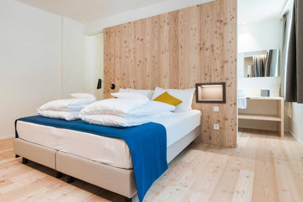 Zimmer mit hellen Holzwänden und Bett mit blauer Decke