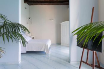 Zimmer mit hellbaluen Fliesenboden, weißem Doppelbett und Pflanzen