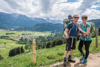 Christian und Jana von A Tasty Hike in Wanderkleidung vor grüner Landschaft und Bergpanorama im Allgäu