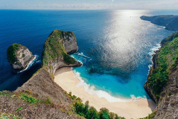 Von Felsen eingeschlossener Kelingking Strand in Bali von oben fotografiert mit Sonnenscheim im klaren türkisblauen Wasser