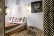 Bett im Schlafzimmer im Riad mit rotgemusterter Decke und weißer Wand
