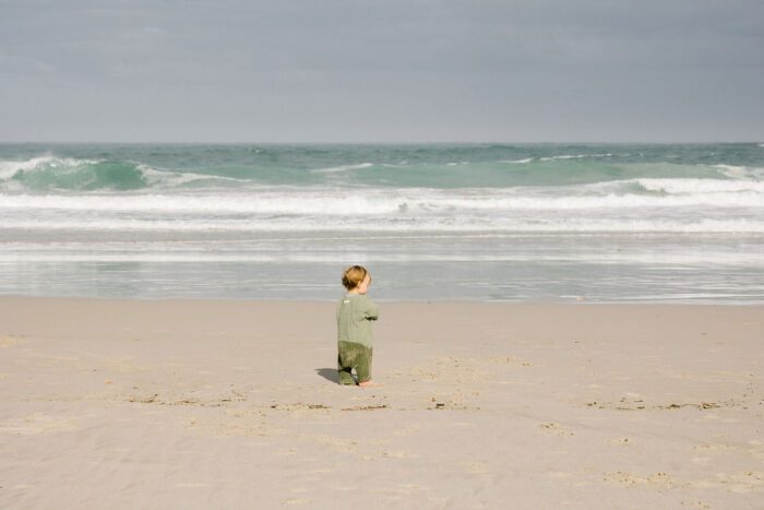 Kleiner Junge an einem Sandstrand mit moderaten Wellen