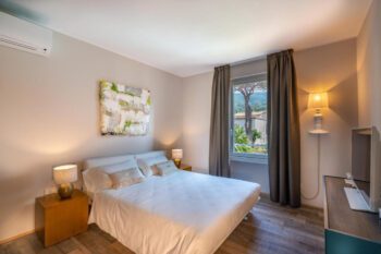Hell eingerichtetes Hotelzimmer mit Doppelbett, Klimaanlage und Blick in Garten