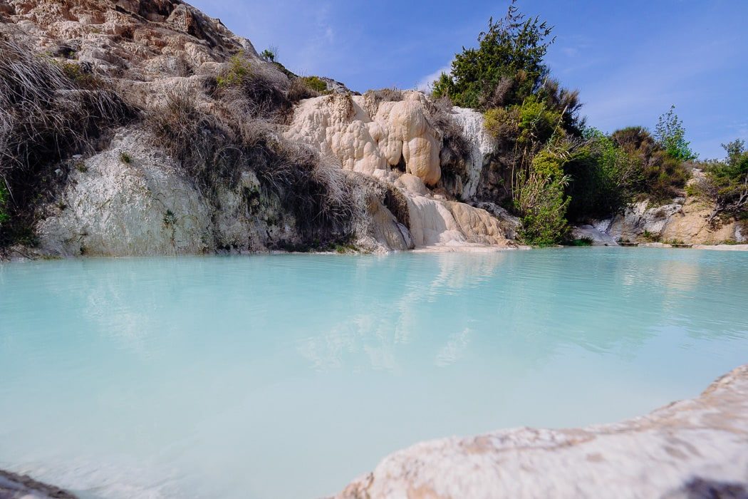 Türkisfarbenes Wasser mit Felsen und Büschen im Hintergrund