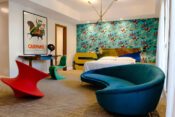 Hotelzimmer mit bunter Tapete, Doppelbett und Retro Sofas in Blau und Rot