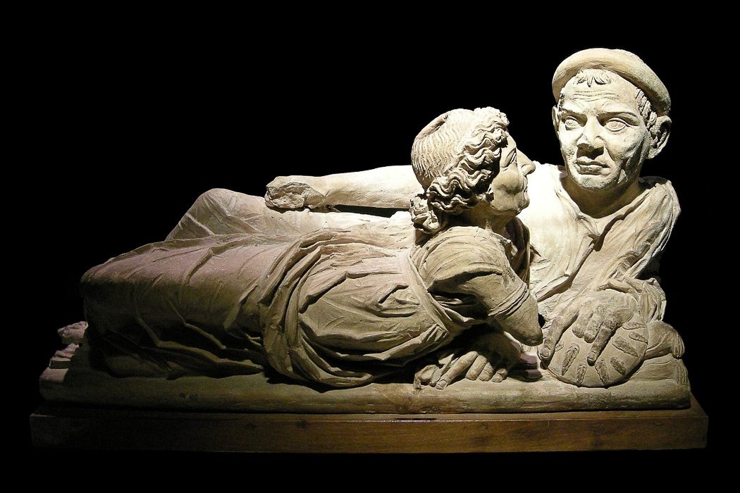 Skulptur aus Stein mit zwei Figuren mit Gesichtern, schwarzer Hintergrund
