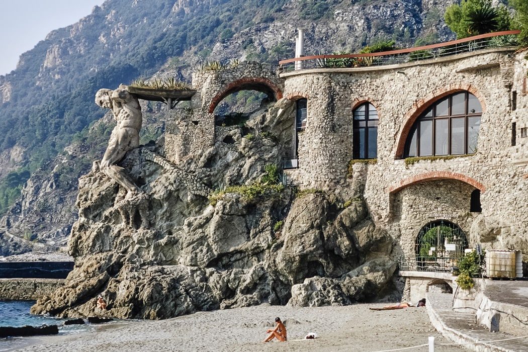 In den Felsen gehauenes Haus mit Skulptur und Strand im Vordergrund