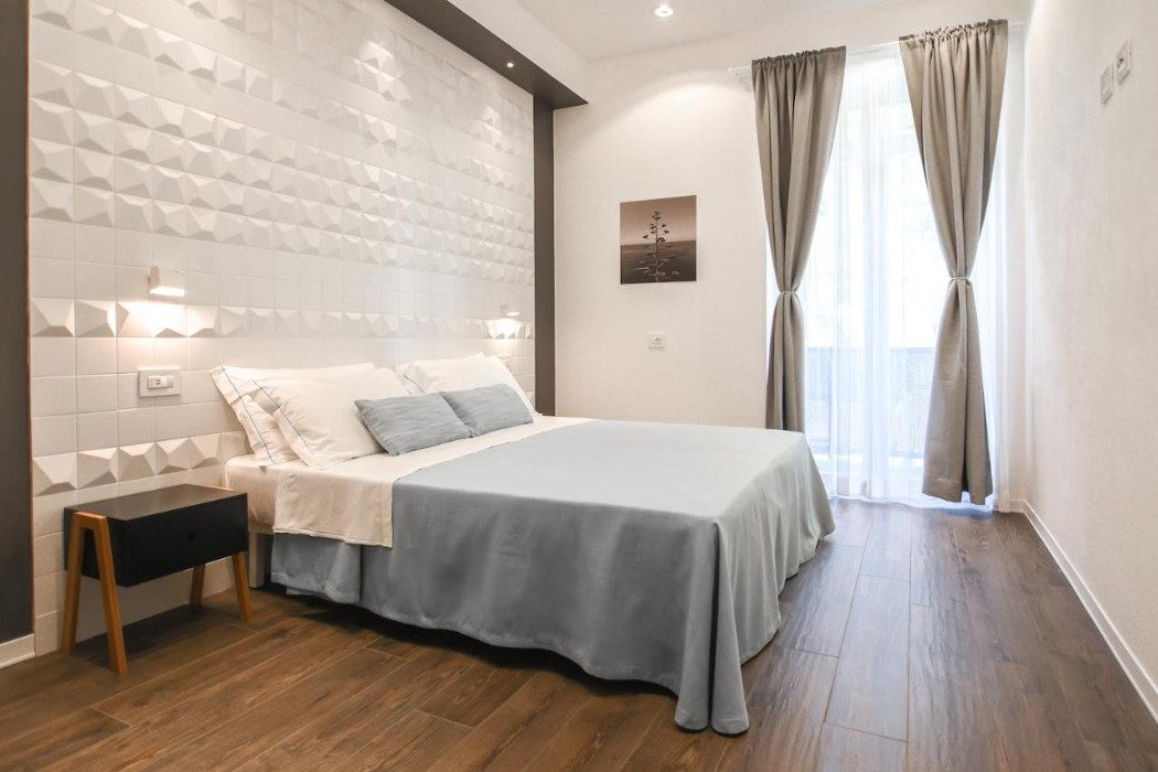 Zimmer mit weißer Wand mit Muster, Doppelbett mit hellblauem Bezug, großes Fenster
