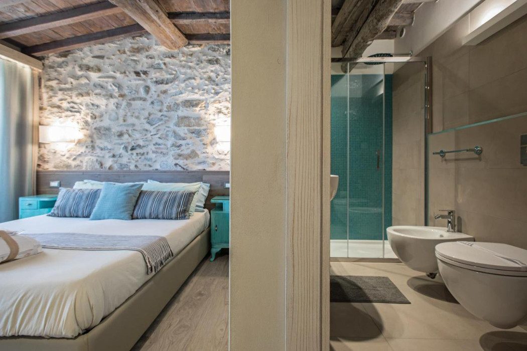 Modernes Doppelbett mit unverputzter Wand, Balkendecke und modernes Badezimmer 