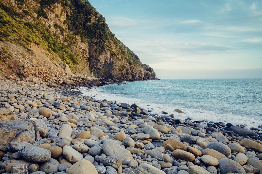 Nahaufnahme von Steinen auf Strand mit Meer und Berg im Hintergrund