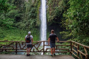 Zwei Männer stehen auf einer Aussichtsplattform und schauen auf den La Fortuna Wasserfall in Costa Rica