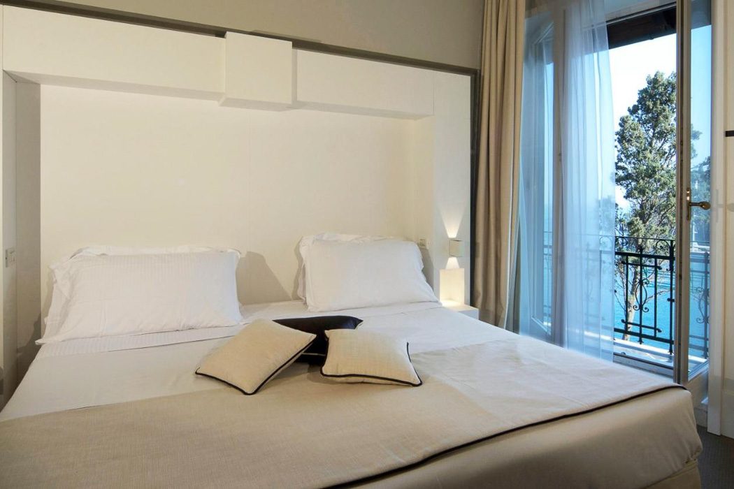 Hotelzimmer mit weißem Doppelbett, modernes Design und Balkon mit Meerblick