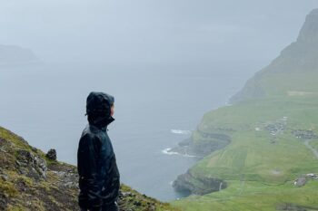 Eine Frau steht mit Regenjacke auf den Färöer Inseln