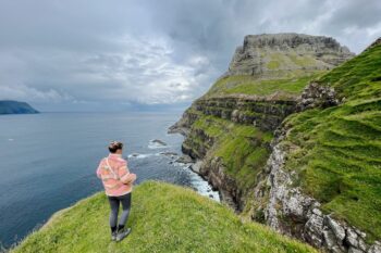Eine Frau steht an einer Klippe bei Gasadalur auf den Färöer Inseln