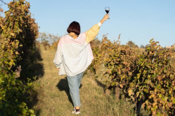 Frau von hinten fotografiert mit Weinglas zwischen Weinreben