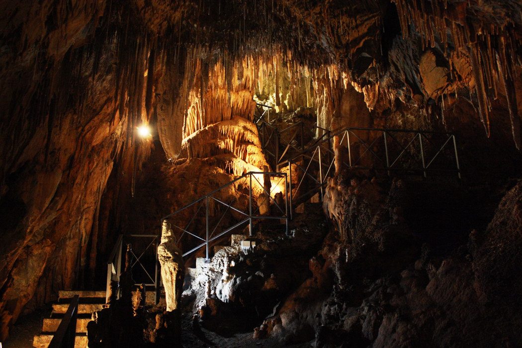 Tropfsteinhöhle mit Metalltreppe und beleuchteten Ecken