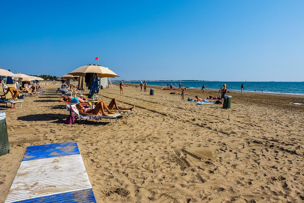 Blick auf goldgelben Strand mit Sonnenschirmen und Liegestühlen und Menschen die sich sonnen