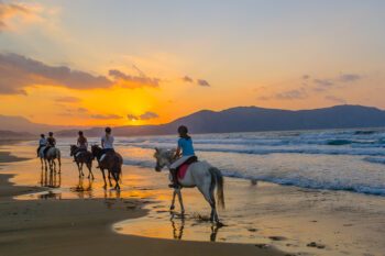 Junge Mädchen reiten bei Sonnenuntergang am Strand von Kreta